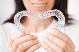 A smiling person holding two clear aligners in a heart shape