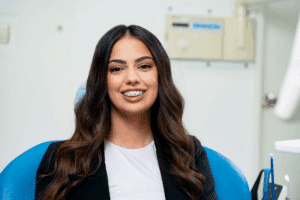 A smiling young woman with braces sitting in an orthodontist's chair, representing a guide on your first orthodontist consultation.