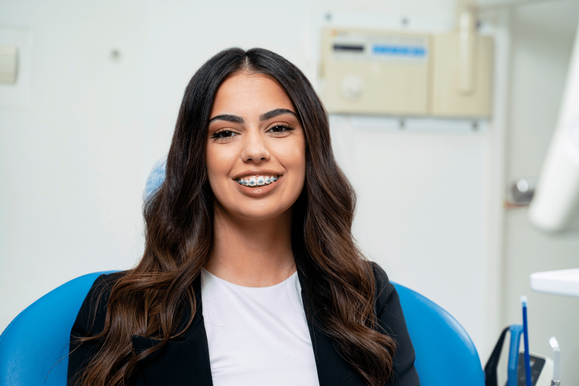 A smiling young woman with braces sitting in an orthodontist's chair, representing a guide on your first orthodontist consultation.