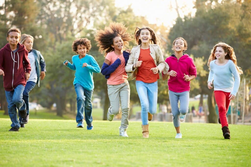 Group of smiling teenagers running together through a sunny park.