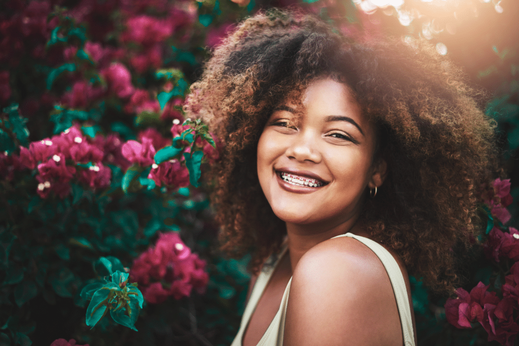 Smiling woman wearing braces outdoors near flowering plants