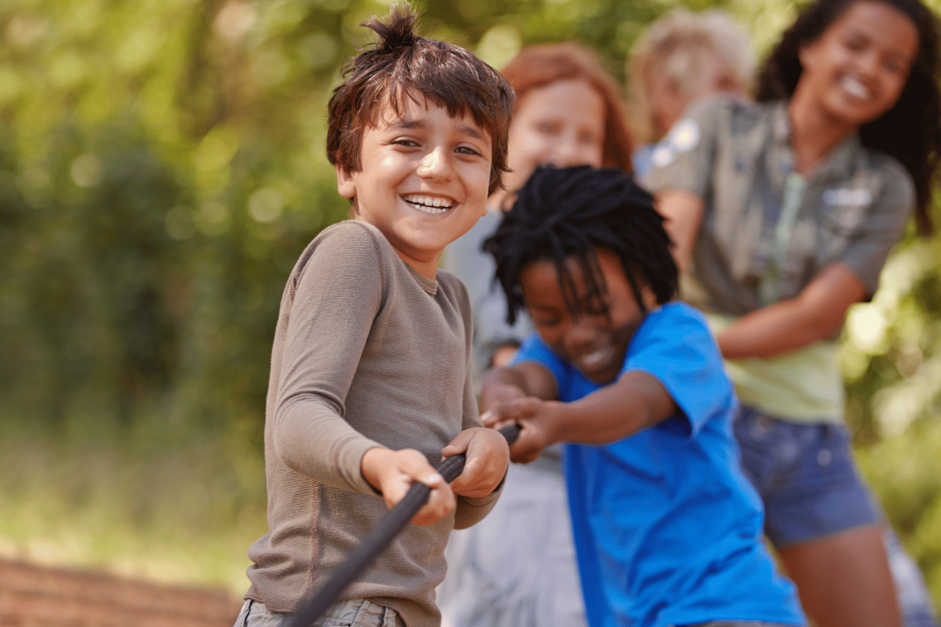 Group of diverse children smiling and playing tug-of-war outdoors